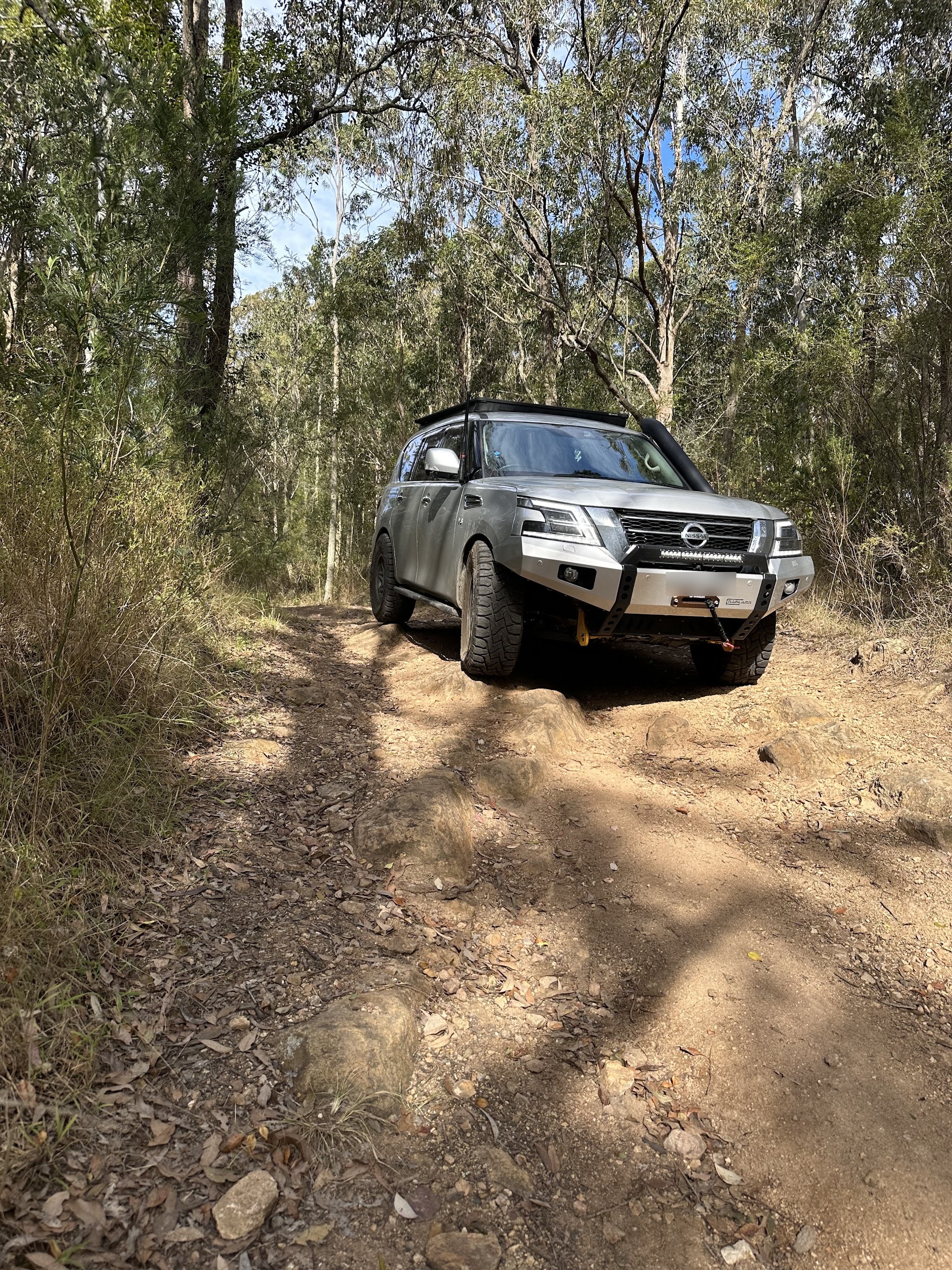 A Nissan Patrol fitted with a bull bar mounted LED light bar, out on a rocky bush track.