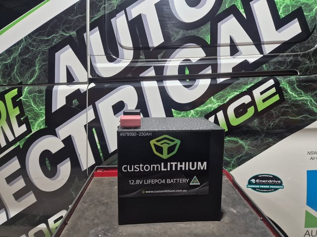 A customLITHIUM 12.8 volt 230 amp hour battery in front of the branded workshop trailer.