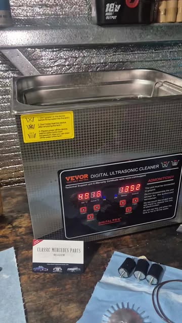 An ultrasonic cleaner on the workshop bench with fuel injectors laid out beside it.